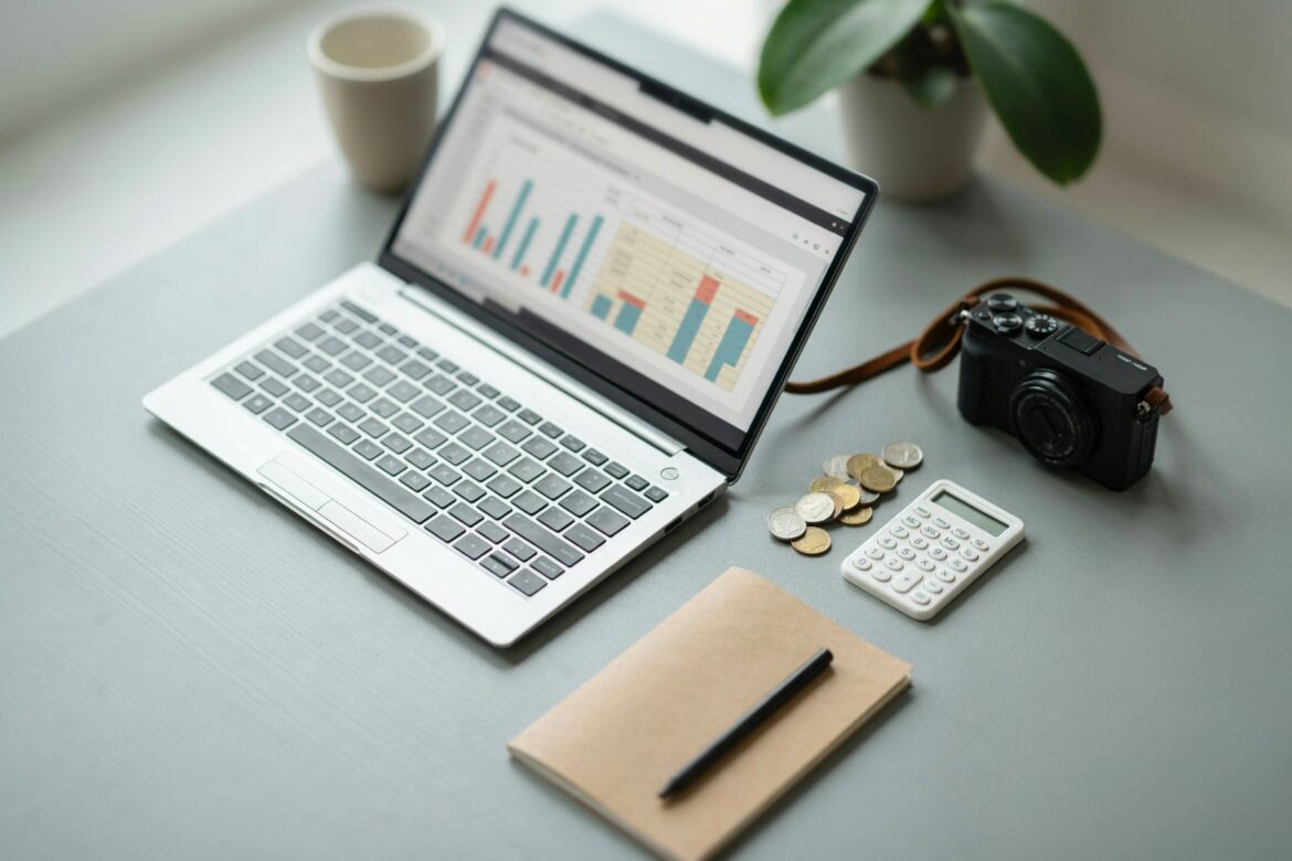 Laptop mit Budget-Tabelle und Diagrammen neben Kamera, Taschenrechner und Münzen