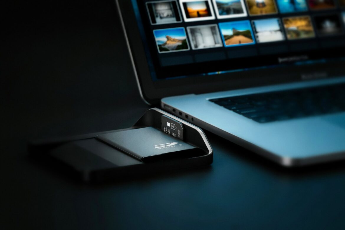 Speicherkarte im Kartenleser neben Laptop mit Foto-Miniaturen