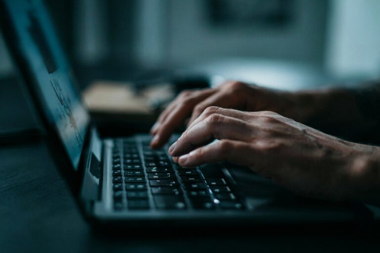 Hände auf Laptop-Tastatur neben Kamera und Notizbuch